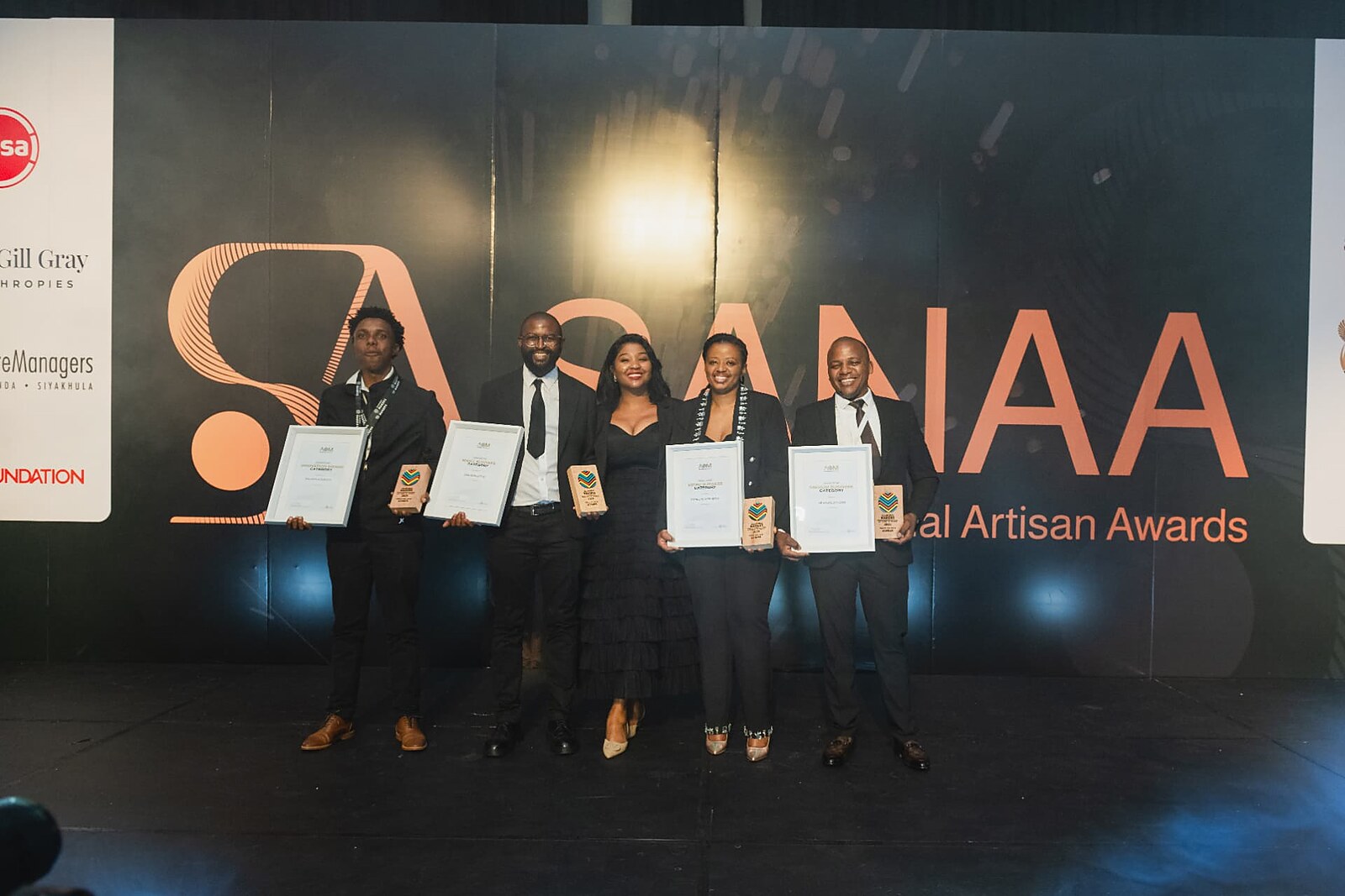 Five category winners lined up with their certificates and trophies in front of the SANAA sponsor wall