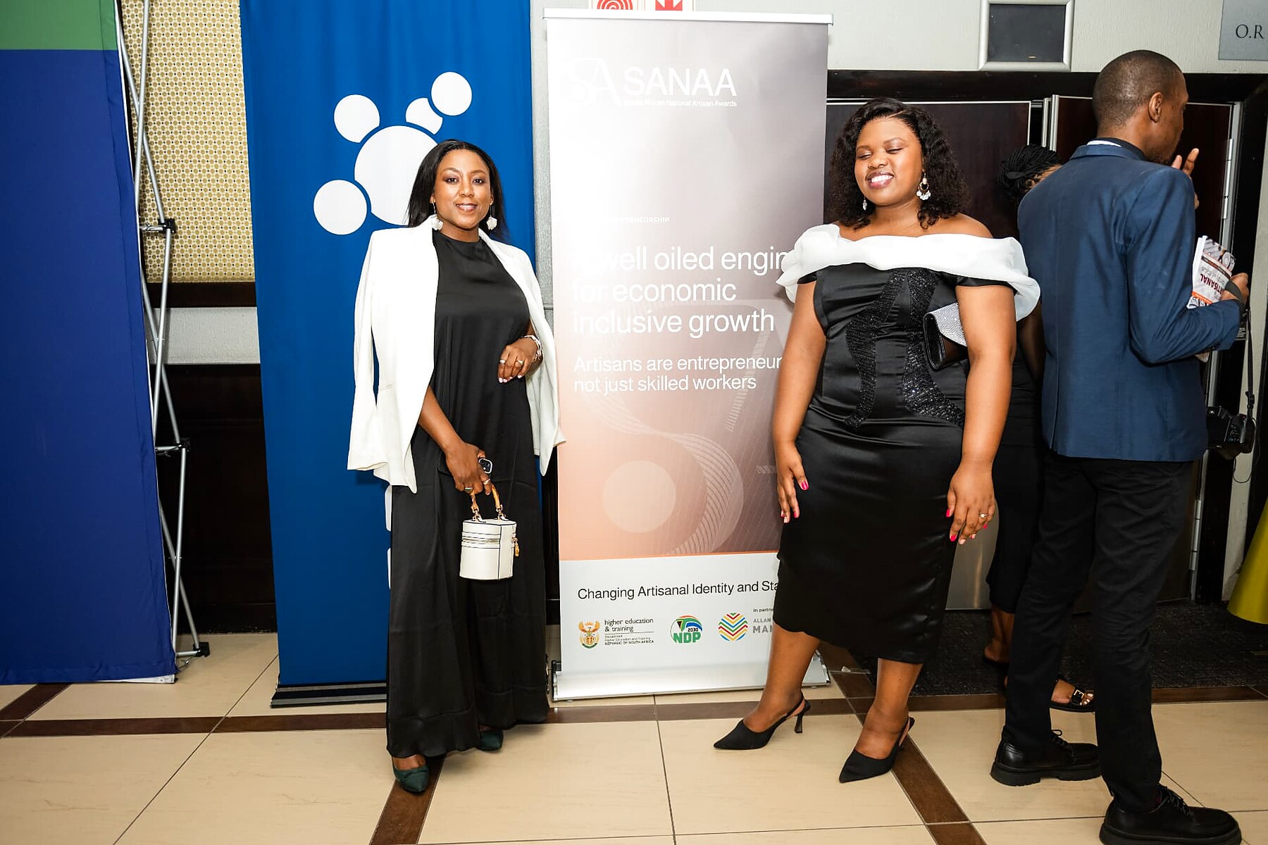 Two guests posing beside the SANAA artisan entrepreneurship banner