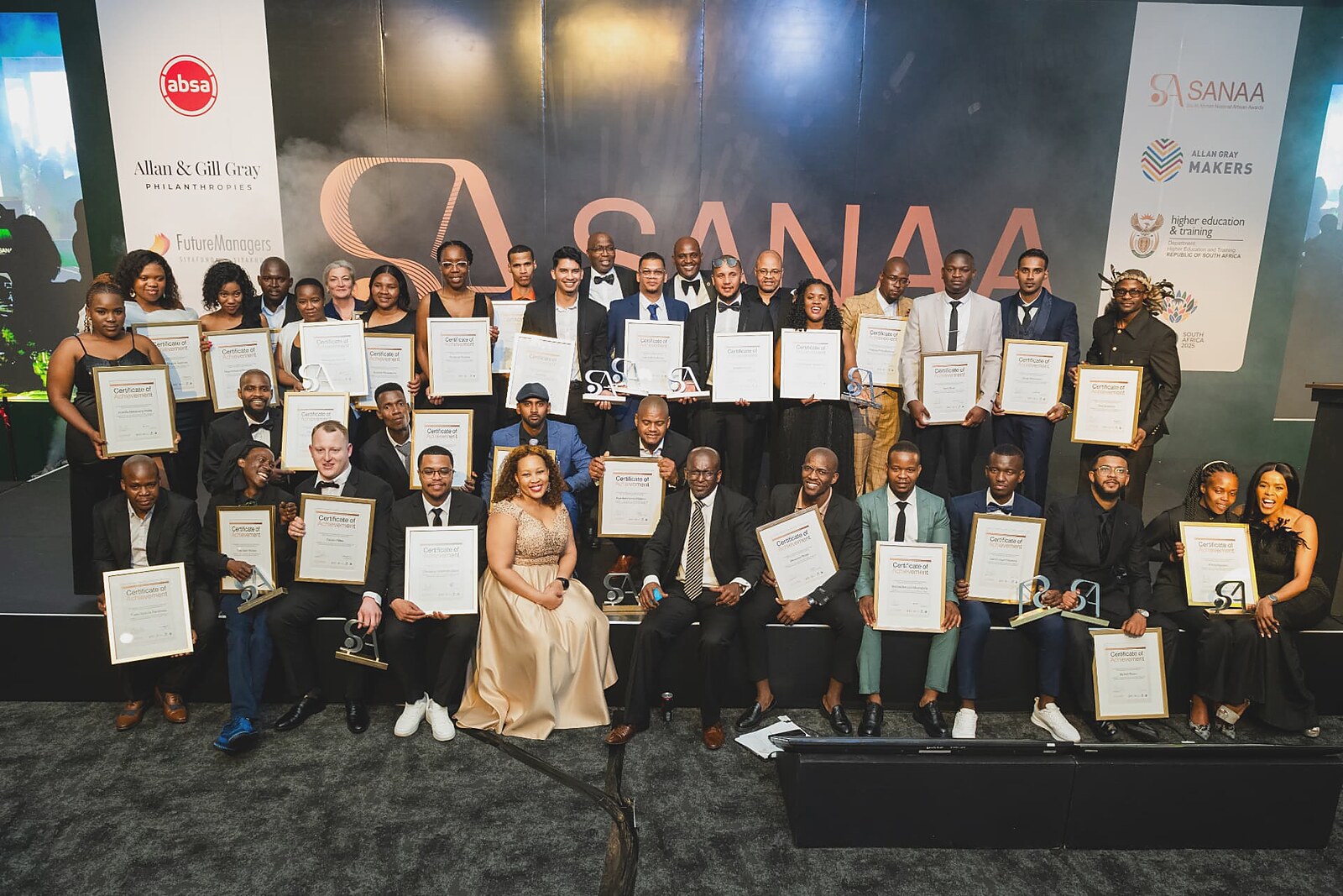 Full group photo of all SANAA 2026 winners holding certificates and trophies on stage