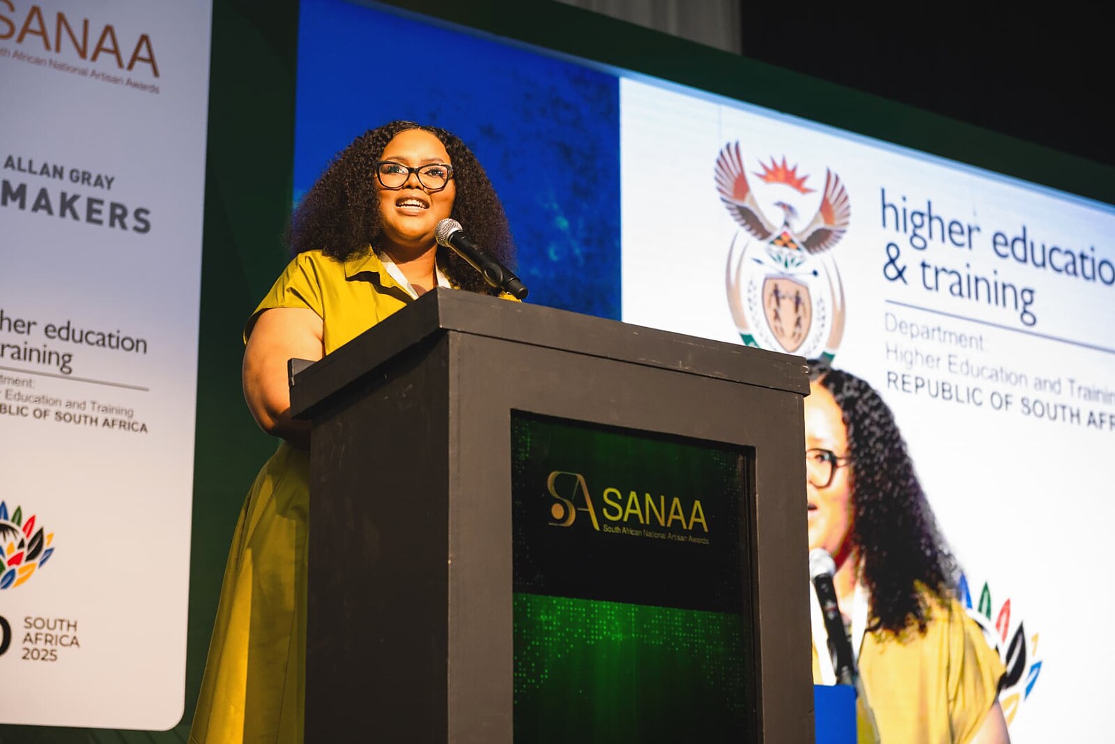 Speaker addressing the gala from the podium in a yellow outfit