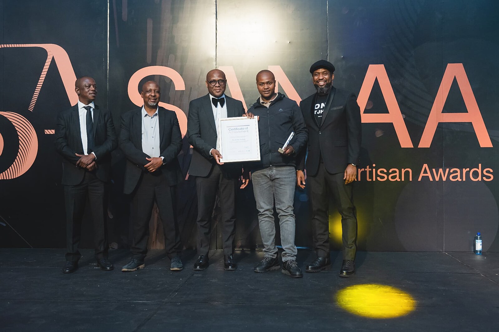 Winner in a black jacket accepting his framed certificate and trophy from the departmental officials