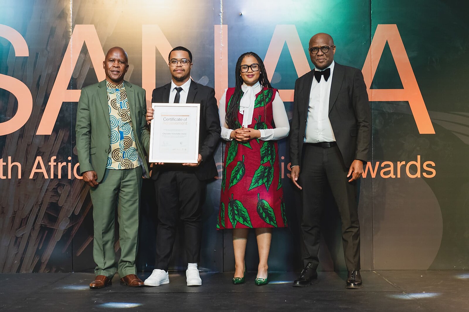 Young artisan in glasses holding his framed Certificate of Achievement with the SANAA panel