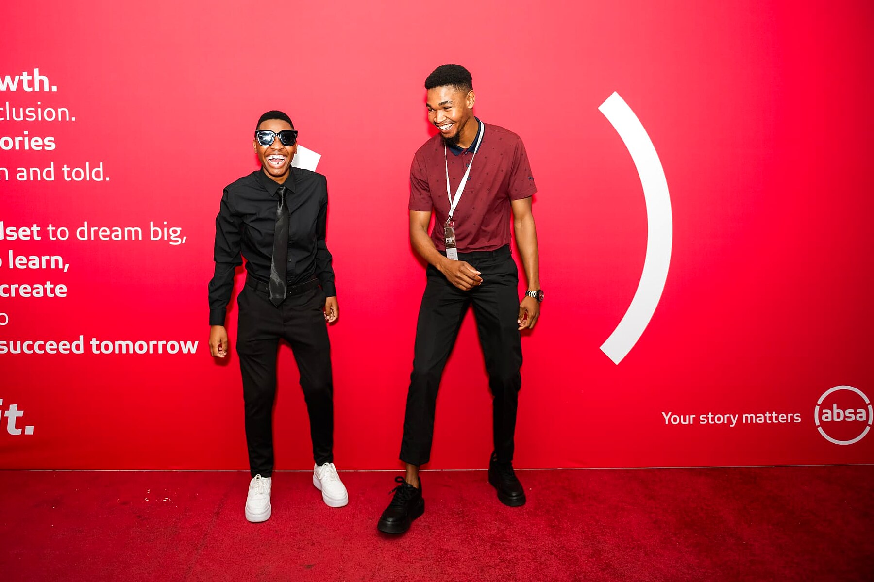 Two young artisans posing playfully on the red carpet at the sponsor wall