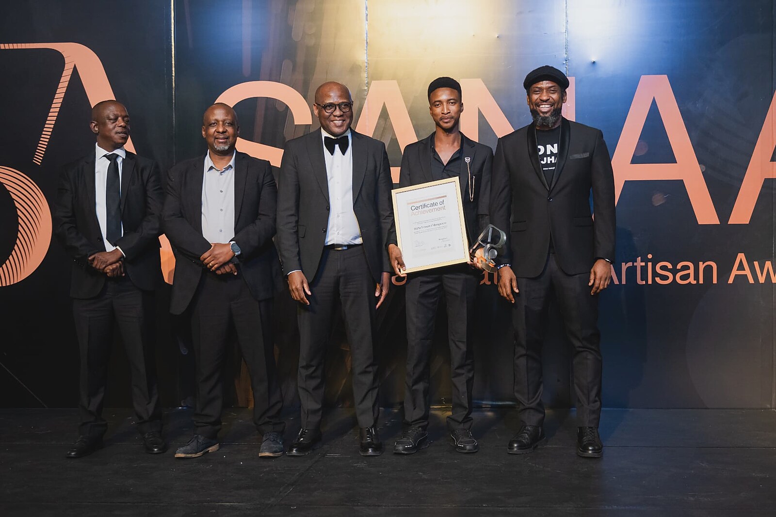 Young artisan receiving his framed Certificate of Achievement and trophy from the SANAA panel