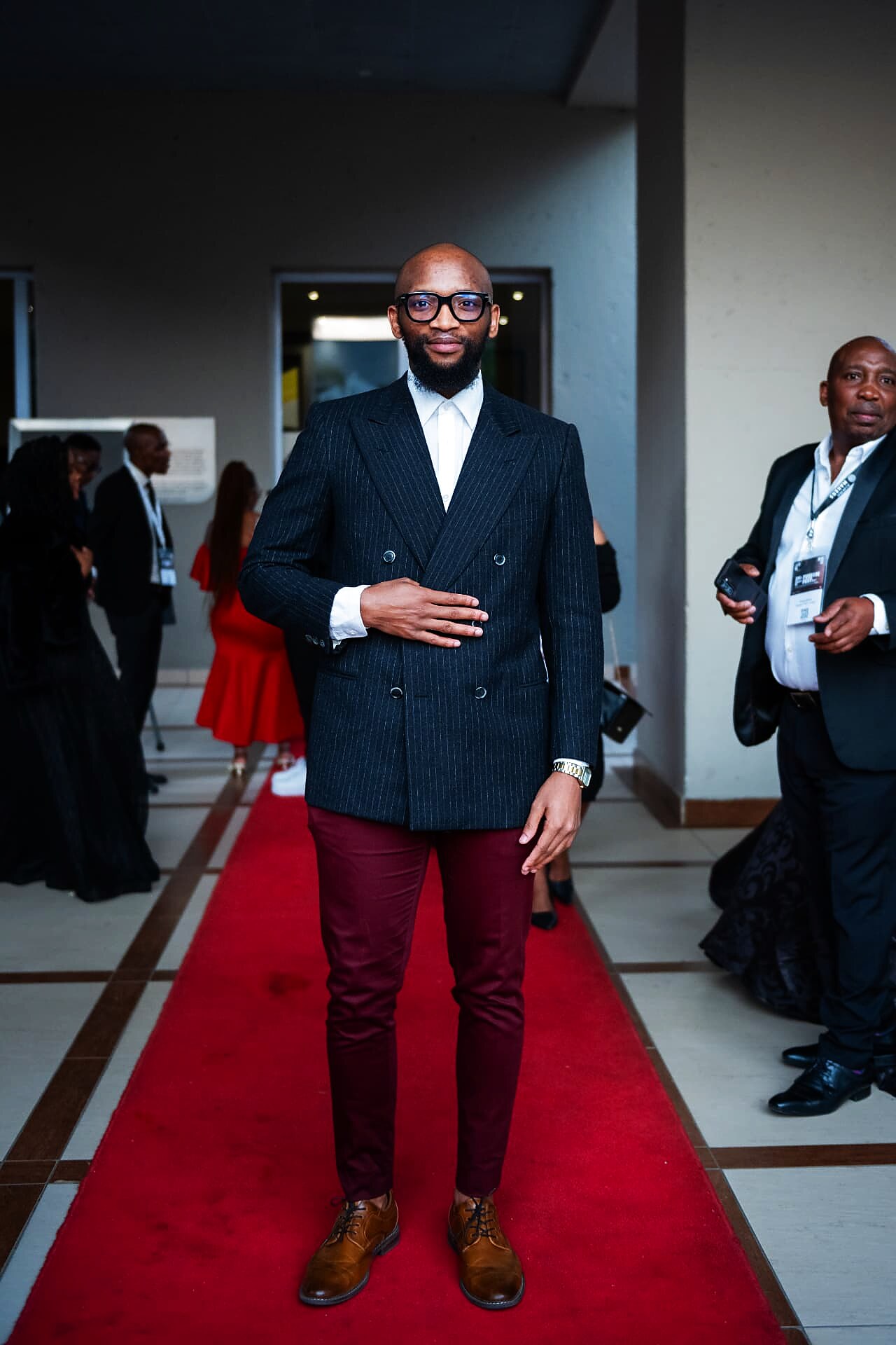 Guest in a pinstripe blazer and burgundy trousers on the SANAA 2026 red carpet