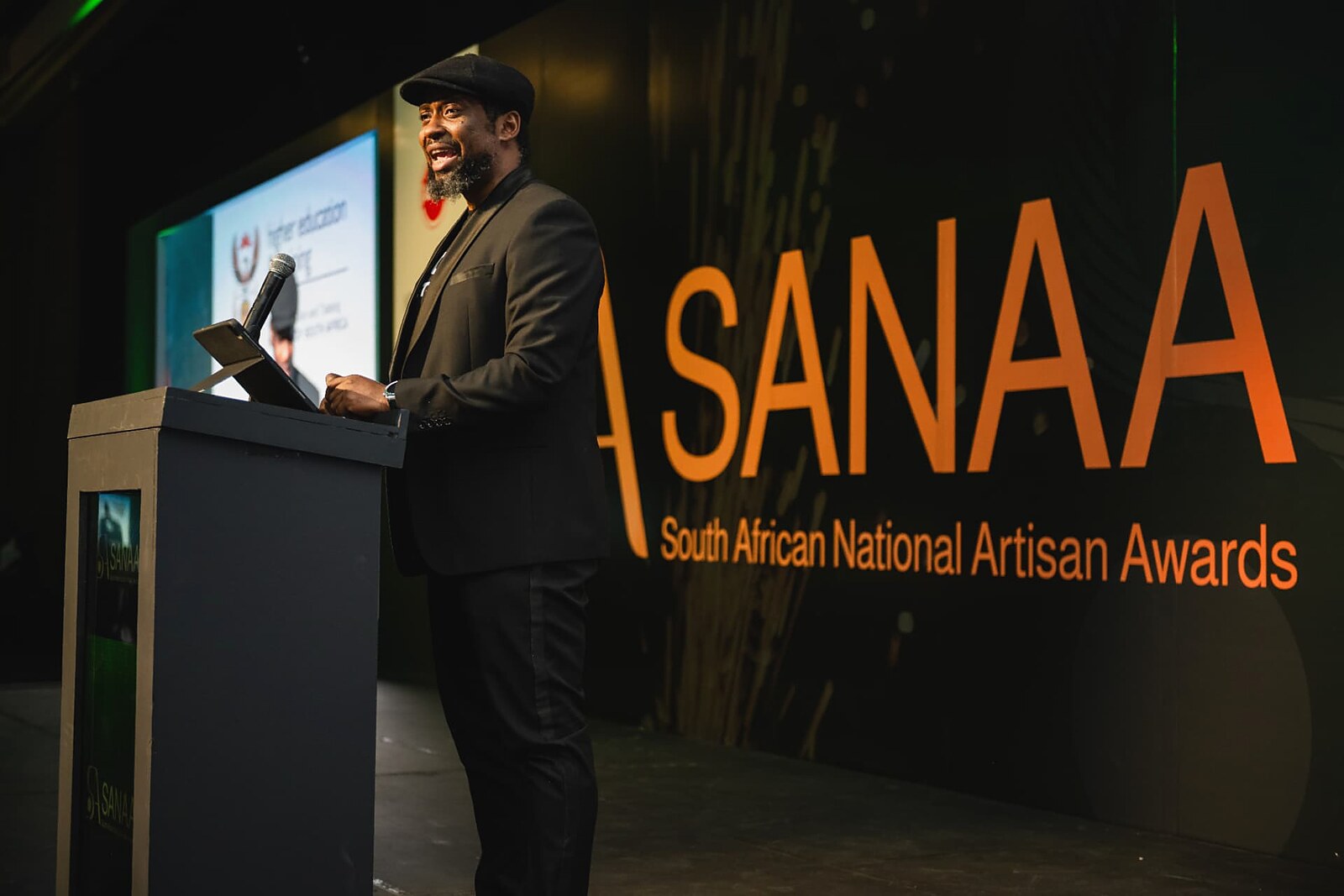MC presenting from the podium in front of the SANAA screen