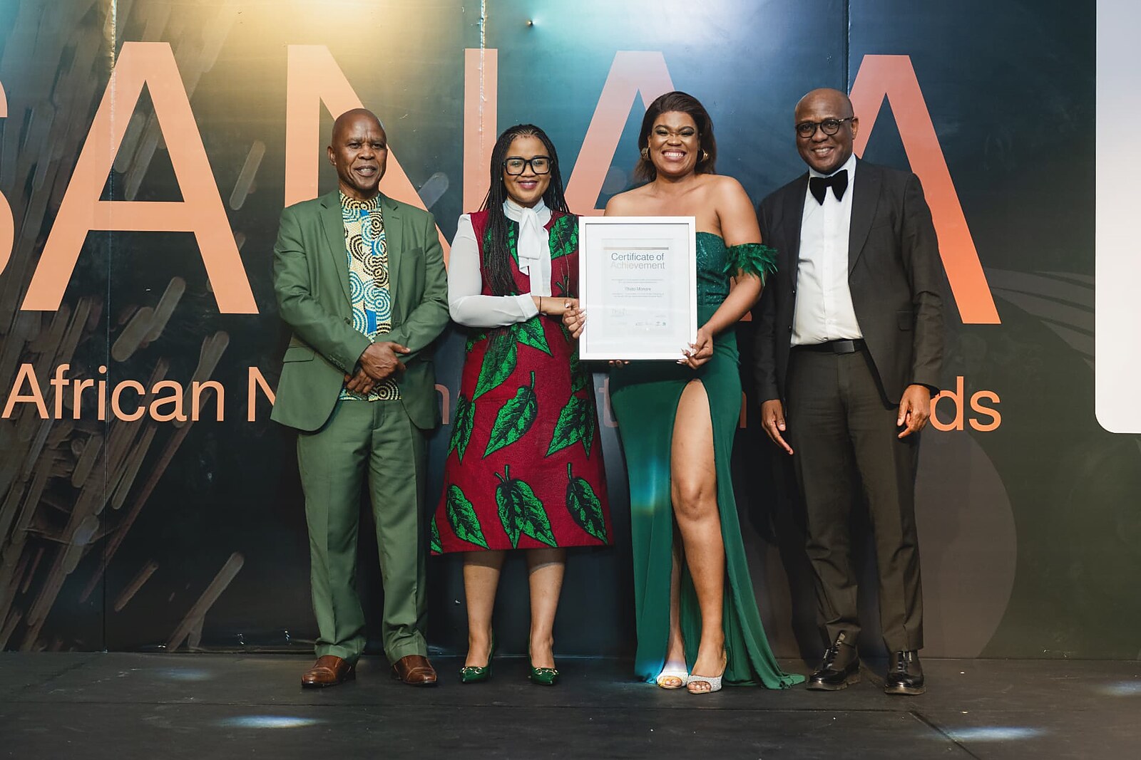Female winner in an emerald gown receiving her framed Certificate of Achievement from officials