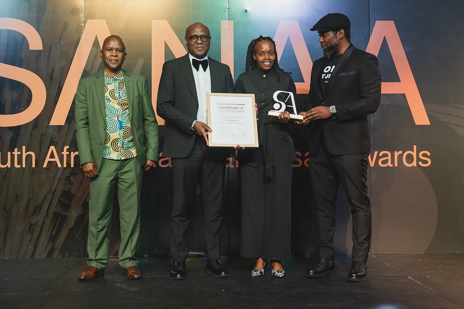 Female winner receiving her framed certificate and SA trophy in front of the full SANAA backdrop