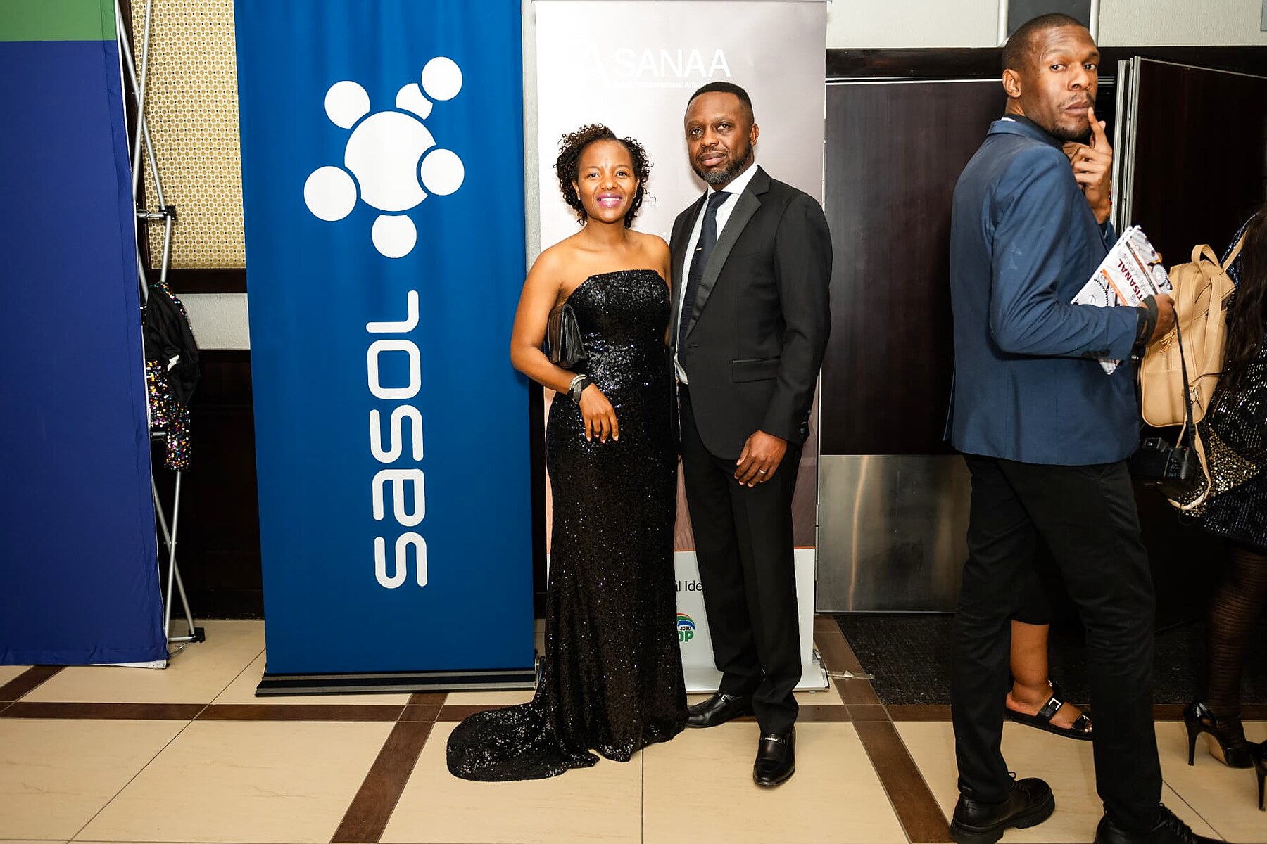 Couple in formal wear posing between the Sasol and SANAA banners