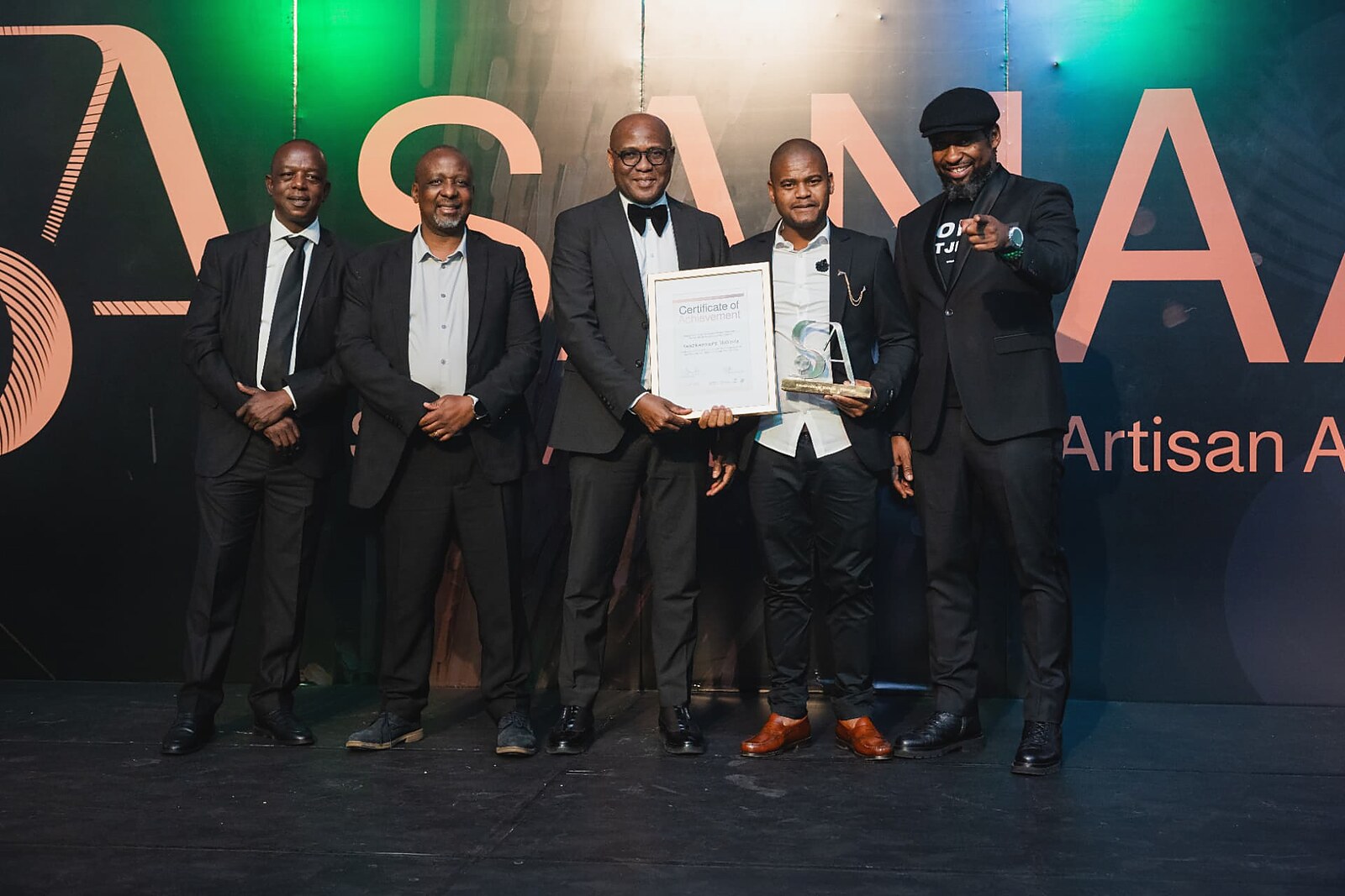 Artisan holding his framed certificate and glass SA trophy with the host pointing in celebration
