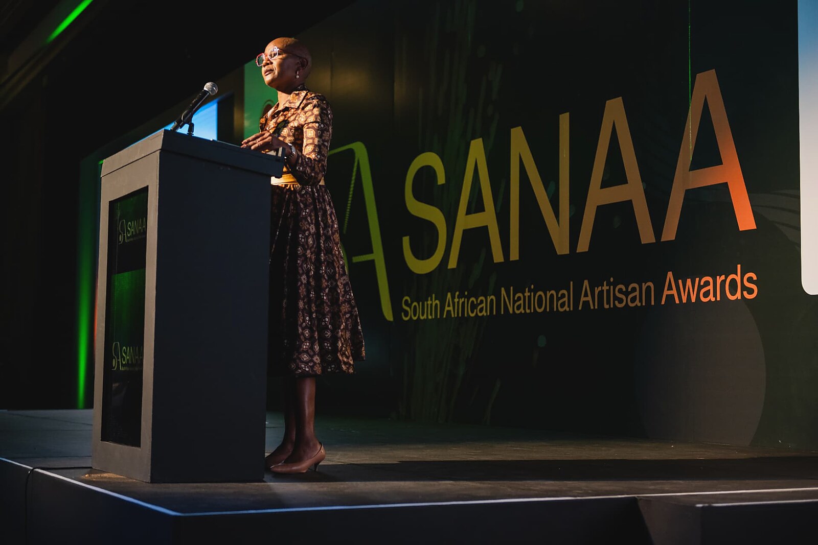 Speaker at the podium beside the illuminated SANAA backdrop