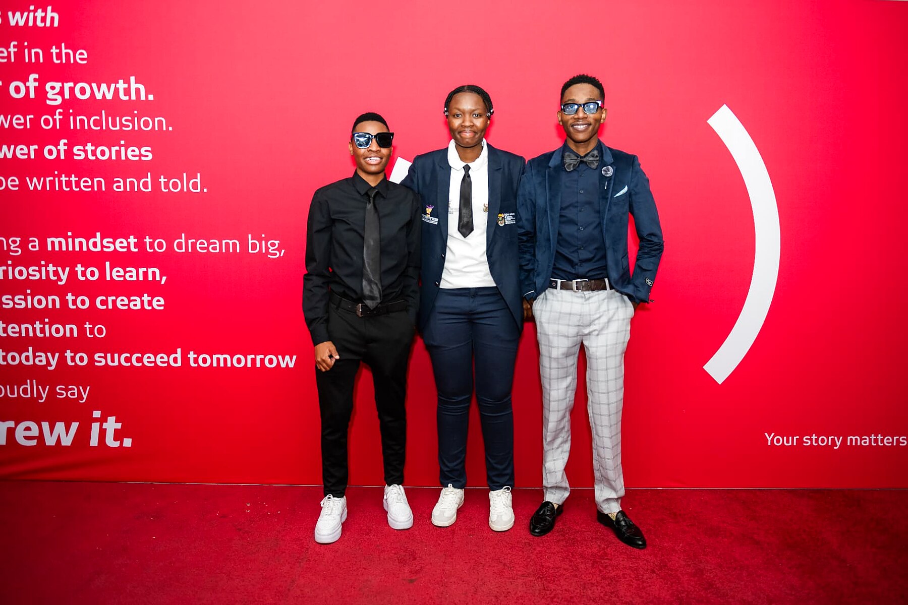 Three young nominees posing together at the sponsor wall on the SANAA 2026 red carpet