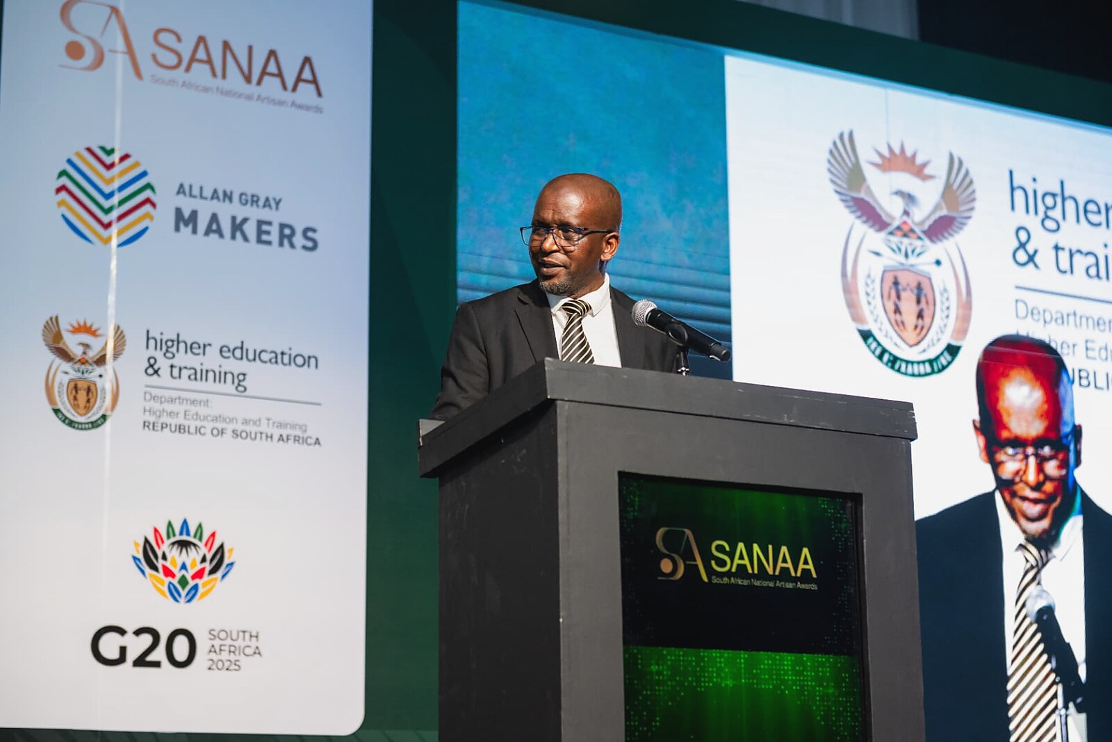 Departmental official addressing guests beside the sponsor banners