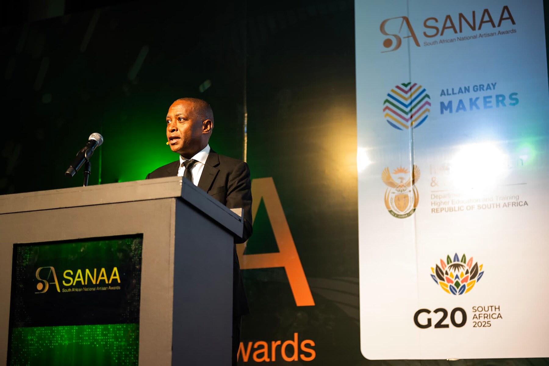 A speaker addressing guests from the podium beside the sponsor banners